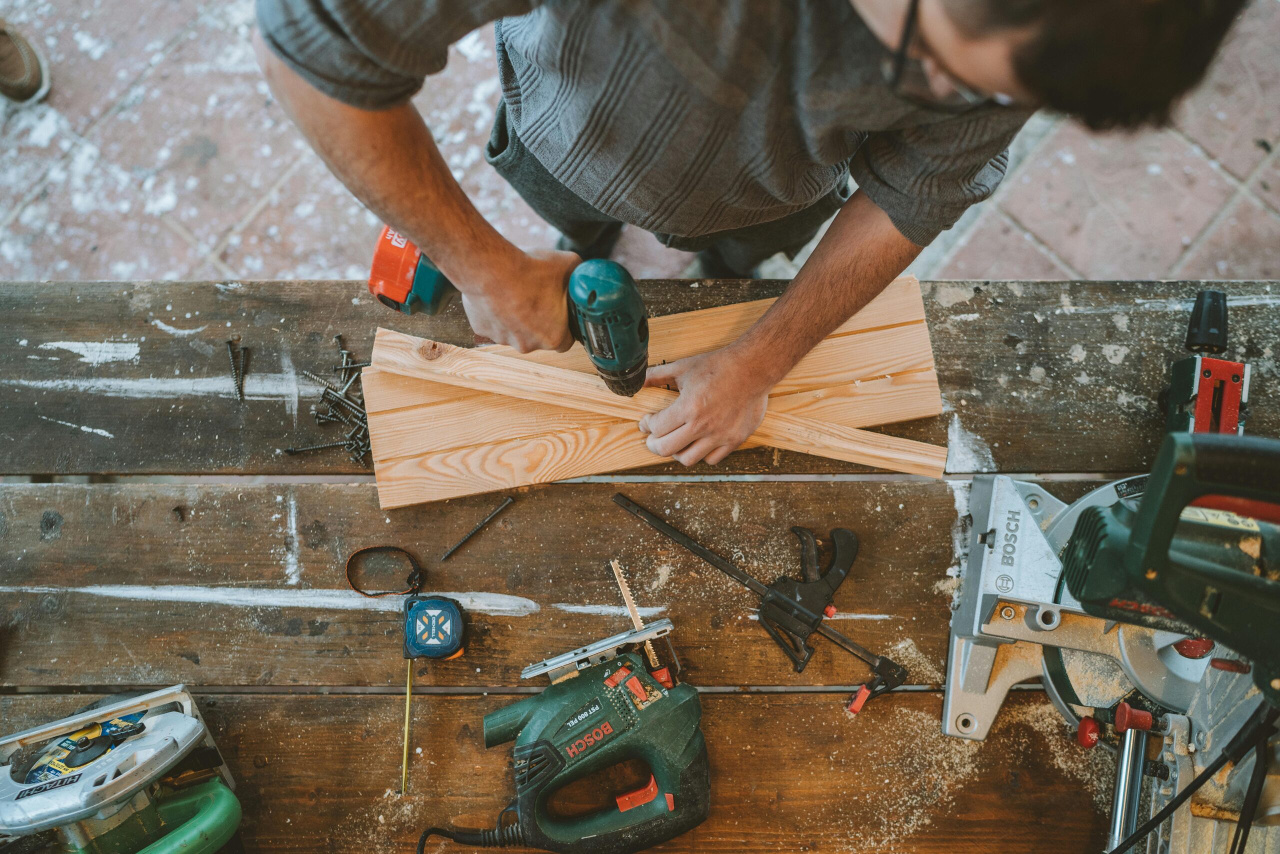 Craftsman busy drilling wooden planks in a carpentry workshop with various tools around.